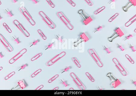 Pink stationery items like paper clips and drawing pins arranged on blue background Stock Photo