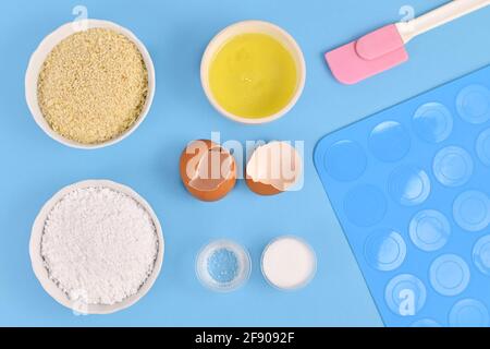 Ingredients for making homemade French Macarons sweets including powdered sugar, ground almonds, egg white, salt and baking tools on blue background Stock Photo