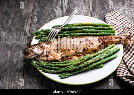 Baked  rainbow trout with asparagus and spices in white plate on wooden table Stock Photo