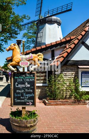 An iconic windmill overlooks Hamlet Square with shops and carousel horse sign for Ice cream in the Danish Village of Solvang, CA Stock Photo