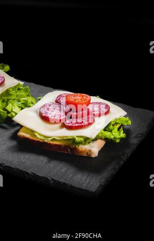 Breakfast sandwiches with dry meat, cheese and lettuce on a black plate Stock Photo