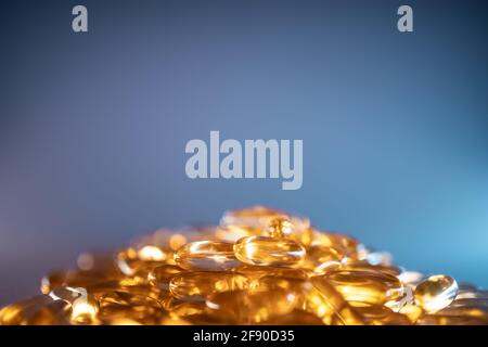 handful of golden fish oil capsules omega 3 vitamins on blue background Stock Photo