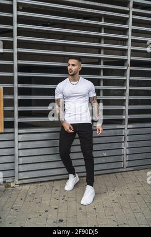 Vertical shot of a young European man with tattooed arms leaning on a gate Stock Photo