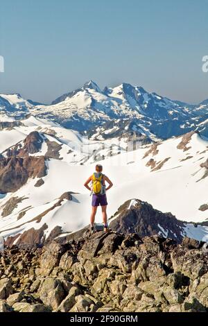 Rear view of attractive fit woman on mountain summit wearing backpack. Stock Photo
