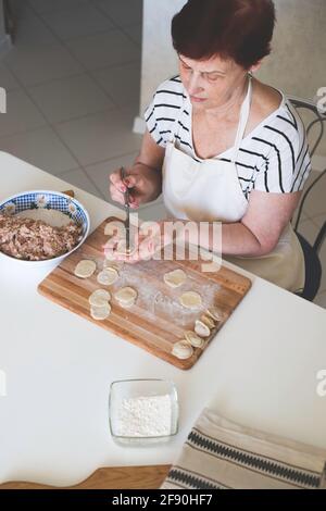 A woman in a white kitchen prepares traditional Russian dumplings from meat and dough Stock Photo