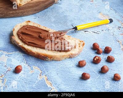 Cutted piece of bread with chocolate paste and hazelnuts, yellow knife Stock Photo