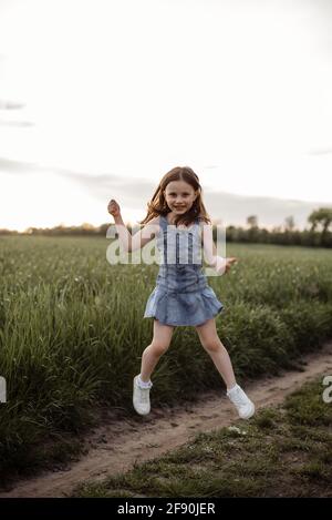 Happy 5 years old girl is jumping in a green field with long hair Stock Photo