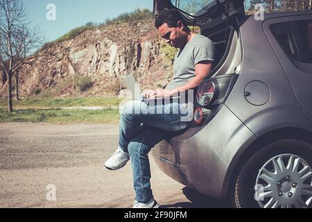 latino man searching on laptop for help sitting in back of car Stock Photo