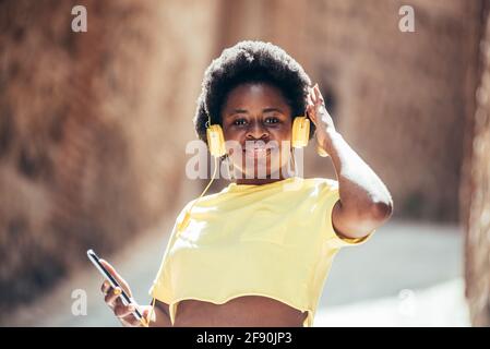 Portrait of a black girl with afro hair listening to music and dancing in an old city street. Stock Photo