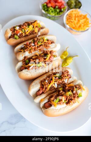 Close up of plate of chili dogs and toppings on white marble counter. Stock Photo