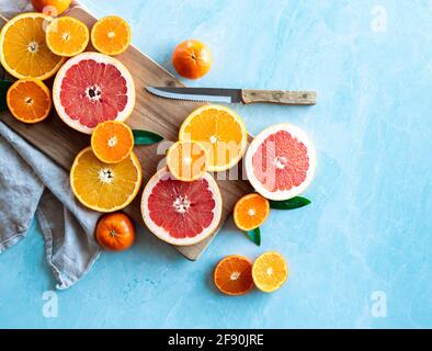 Slices of various citrus fruit on cutting board on blue background. Stock Photo