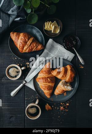 Plates of croissants with coffee and jam on black table from above. Stock Photo