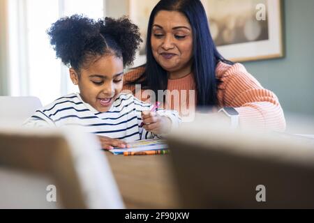 Smiling grandmother guiding granddaughter coloring with crayons in book Stock Photo