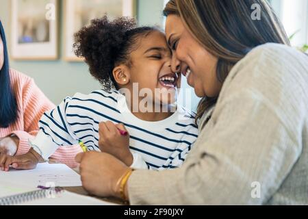 Cheerful daughter rubbing nose with mother while learning drawing at home