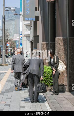 Japanese male and female office workers bowing (ojigi) with each other on the pavement, Ginza, Tokyo, Japan Stock Photo