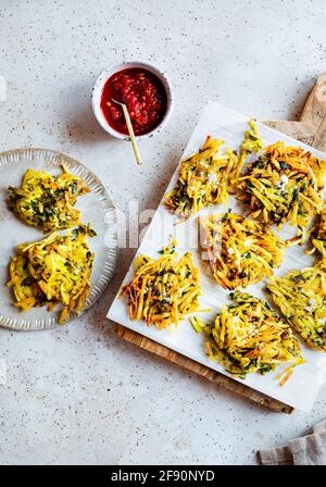 A flatlay of Moroccan Hashbrowns on a wood board, served with harissa sauce. A small plate of hashbrowns to the left. Stock Photo