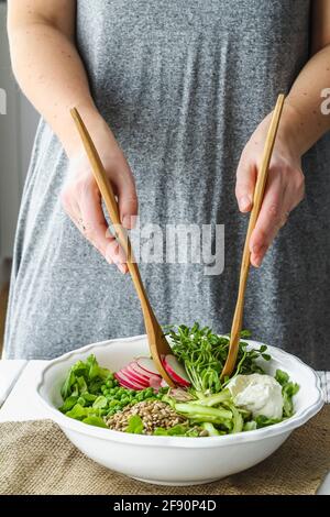 Female hands using wooden salad spoons to toss fresh spring salad Stock Photo