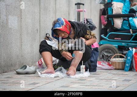 Homeless Japanese female sits on ground shaving legs in public, Harajuku, Tokyo, Japan Stock Photo