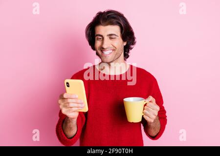 Portrait of attractive cheerful glad guy drinking beverage using device isolated over pink color background Stock Photo