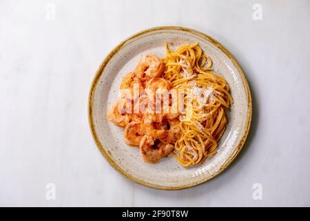 Tomato spaghetti pasta with shrimps prawns in sauce and parmesan cheese served in spotted ceramic plate over white marble background. Flat lay, copy s Stock Photo