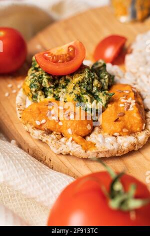 Crispy puffed rice cakes on table with hummus spread spinach with eggs and tomato and vegetables on the table - top view on healthy vegetarian breakfa Stock Photo