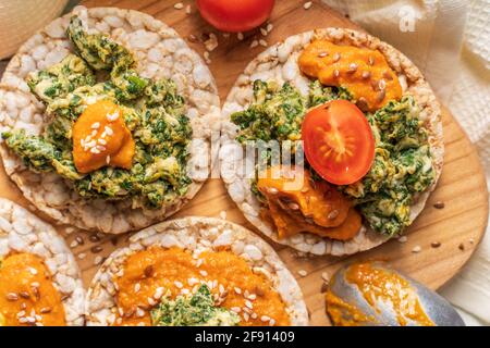 Crispy puffed rice cakes on table with hummus spread spinach with eggs and tomato and vegetables on the table - top view on healthy vegetarian breakfa Stock Photo