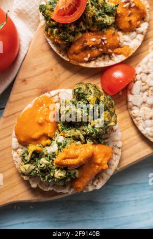 Crispy puffed rice cakes on table with hummus spread spinach with eggs and tomato and vegetables on the table - top view on healthy vegetarian breakfa Stock Photo