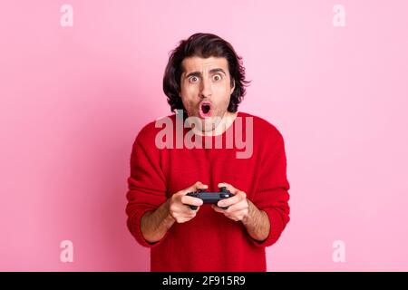Photo portrait of shocked man holding videogame controller in two hands isolated on pastel pink colored background Stock Photo