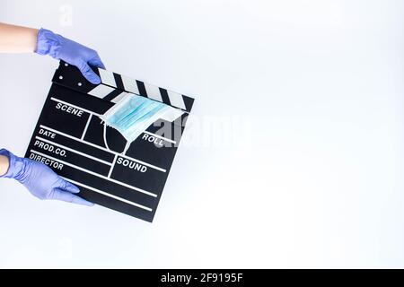 Woman in blue disposable rubber gloves holding movie clapper. Influence of pandemic on cinematography Stock Photo