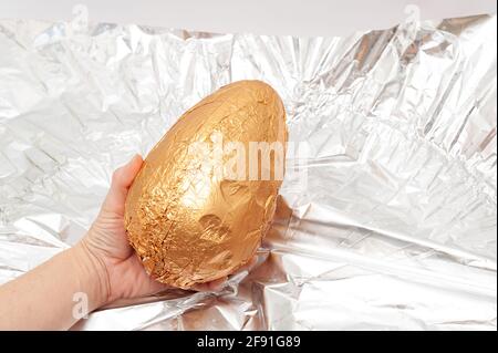 Easter Egg - Hand holding homemade chocolate egg in golden packaging. Stock Photo