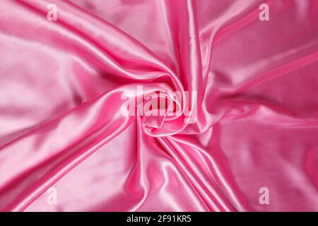 Colored pink textile satin fabric folded in folds and waves with highlights and texture shimmers in the light Stock Photo