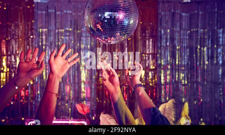 Disco dancing underneath the disco ball with hands in the air.