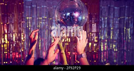 Crowd of people with hands in the air on the dance floor dancing underneath a disco ball.