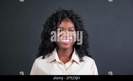 Attractive young African-American woman with curly hair smiles and laughs looking into camera on black background in studio close view Stock Photo