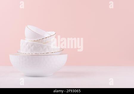 White ceramic crockery stack with golden bezel, different texture on white wooden table, soft light pastel pink wall, elegant delicate kitchen interio Stock Photo