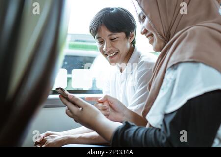 a smiling young Muslim couple looking at the cellphone screen together Stock Photo