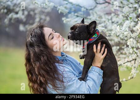 Beautiful young woman playing with bulldog outdoors. Cute hipster girl hugs and kissed her dog. Stock Photo