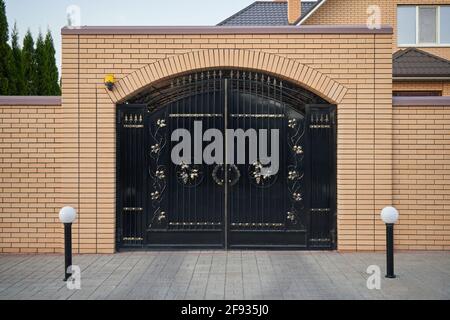 High brick fence and black metal gates Stock Photo