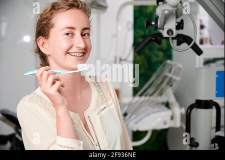 Young woman with metal braces on teeth holding toothbrush with toothpaste. Woman with orthodontic brackets on teeth demonstrating oral hygiene instrument for cleaning teeth. Concept of hygiene. Stock Photo