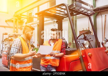 Two workers talk about an order in front of forklifts in the warehouse Stock Photo