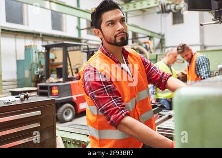Metal worker in the production of the metal factory operates a machine using a large wheel Stock Photo