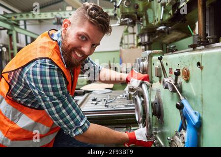 Smiling worker in metal factory operates drill press on a large wheel Stock Photo
