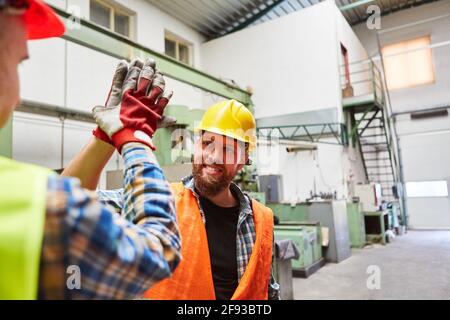 Two workers greet each other with high five in the metalworking factory Stock Photo