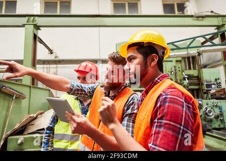 Group of industrial workers using tablet computer while planning orders in a factory hall Stock Photo