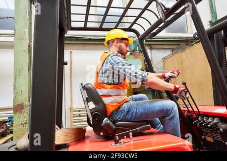 Warehouse worker as a forklift driver while driving a forklift in the warehouse of the factory Stock Photo