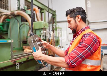 Worker operates a crane control in the warehouse or in the metal processing factory Stock Photo