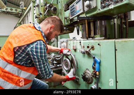Worker in metal processing factory operates drill press on a large wheel Stock Photo