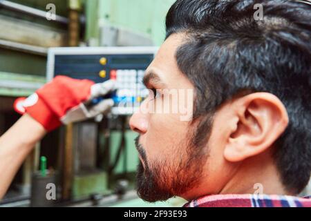 Metal worker at the control panel of a CNC machine for production control in the factory Stock Photo