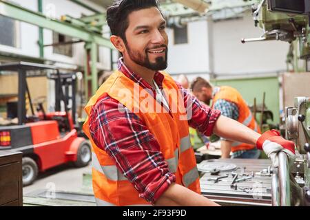 Machinist in the workshop of the metal factory operates a wheel on a drill press Stock Photo