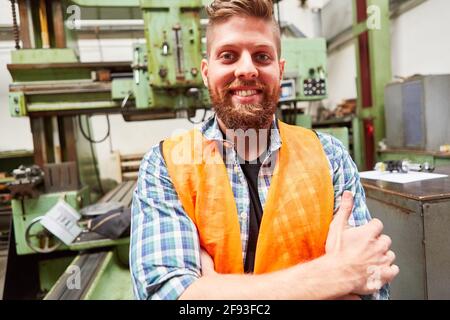 Young man as a proud metalworker apprentice with folded arms in the workshop Stock Photo